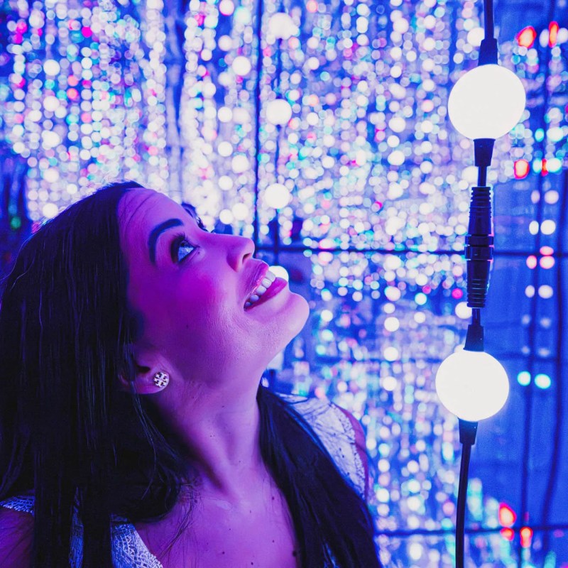 Woman smiling among colorful, glowing lights in a dark space.