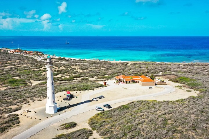 Aerial view of a coastal lighthouse near the ocean with clear skies.
